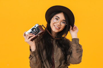 Image of brunette asian tourist woman wearing hat using retro camera