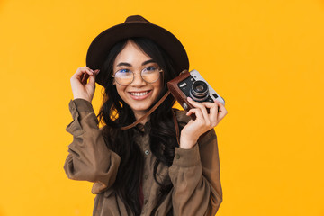 Image of brunette asian tourist woman wearing hat using retro camera