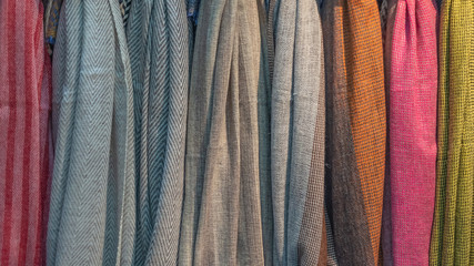 Fabric scarves and shawls of different colors, textures and patterns are hung vertically. Background image.