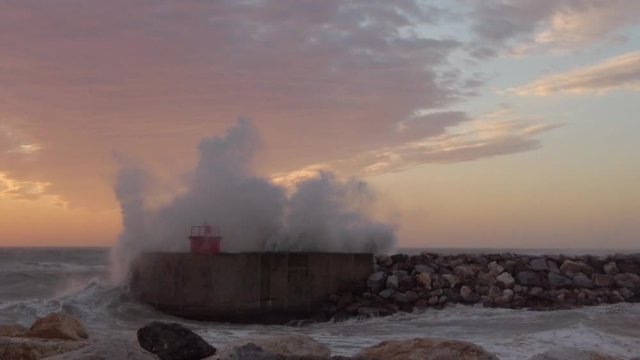 Schizzi e spruzzi del mare che si infrangono sul faro del porto al tramonto. Super slow motion.