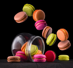 Flying french colorful macaroons and jar on wooden table isolated on black