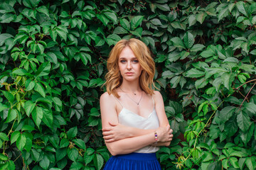 Portrait of a young beautiful woman, standing next to the wall of wild grape leaves.