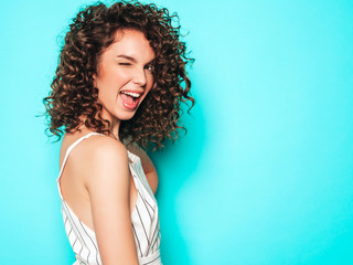 Portrait of beautiful smiling model with afro curls hairstyle dressed in summer hipster clothes.Sexy carefree girl posing near blue wall.Trendy funny and positive woman