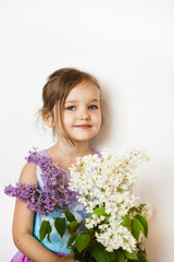 A little girl on a white background stands and holds branches of lilac, blooming kurst, lilac, spring and summer