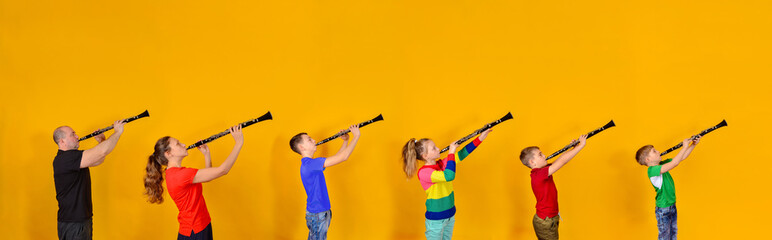 The family plays the clarinet. Father, mother and four children with clarinet on a yellow background. A wide-angle photo of six people with musical themes, panorama. © andov