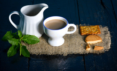 A cup of tea with tasty biscuits, teapot and fresh Leaves on old wooden dark background