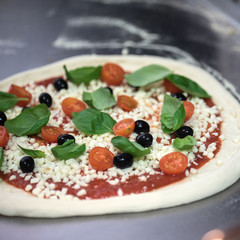 Cook in the kitchen putting the ingredients on the pizza. Pizza food concept.