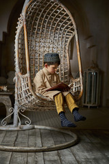 Obraz na płótnie Canvas Little muslim boy in arabic clothes with rosary beads reading holy quran book praying to Allah, ramadan kareem concept kid spiritual peaceful moment inside eastern traditional interior