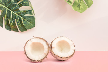 Two halves of fresh raw coconut  on pink backgound with green monstera leaves on white. Trendy concept
