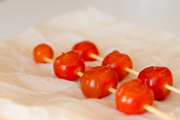 fried cherry tomatoes on skewers and paper on a white background. concept of fresh vegetables and healthy food. BBQ. space for text. top view of tomatoes. the harvest is ripe.