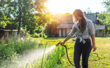 Hipster young woman watering plants a country house, summer and garden care, organic products,...