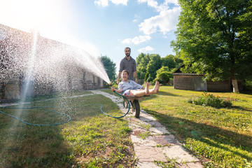 Young happy couple watering garden, a girl with a hose in hand on a trolley, spring and summer...