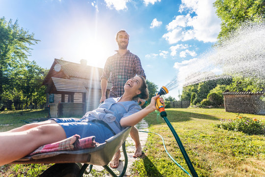 Young happy couple watering garden, a girl with a hose in hand on a trolley, spring and summer concept, eco-friendly lifestyle