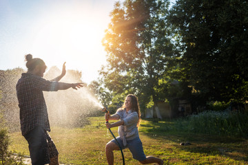 young happy beautiful couple hosing in the garden, summer happiness and love concept, poured water...