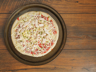 Fresh uncooked chicken pizza on a metal trey ready for cooking, Italian style dish with cheese and tomato sous. Top view.