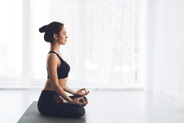 Zijaanzicht van een slank meisje dat yoga beoefent, zittend op de mat