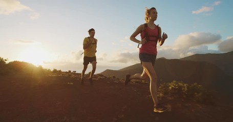 Two adventurous runners exploring a mountain top at sunset, a young athletic couple training outdoors together for a marathon