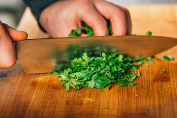 Chef Holding a Knife and Cutting Parsley on a Wooden Cutting Board