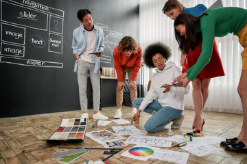 Team job. Group of professional team of interior designers discussing sketches, choosing colors from palettes lying on the floor in the modern office. Creative agency