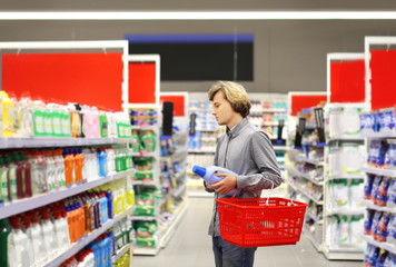 Man shopping in supermarket reading product information.(washing powder,detergent)	