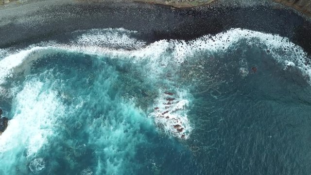 Aerial top view waves break on dark sand near beach.