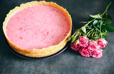 Raspberry cheesecake with rose flowers. Tasty present for Valentine's holiday or Mother's day. Beautiful flat lay on the kitchen. Pink colours on handmade dessert.