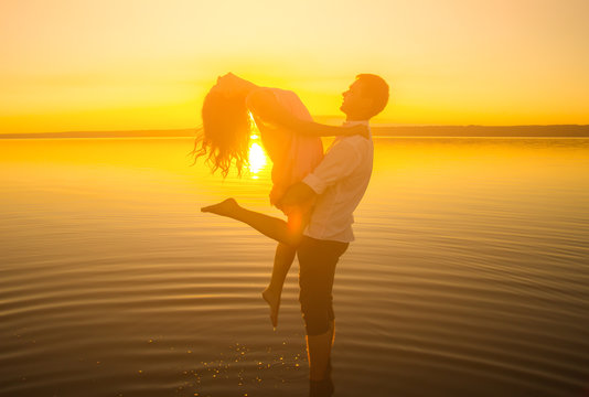 Young couple is dancing in the water on summer beach. Sunset over the sea.Two silhouettes against the sun. Just married couple is hugging. Romantic love story. Man and woman in holiday honeymoon trip.
