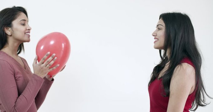 Young female lovers come together with red heart shaped balloons with each other on a date as they flirt and play teasing games while stealing lustful glances at each other, handheld 60fps slow-motion
