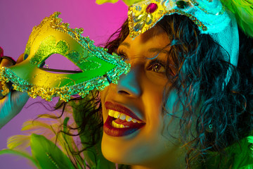 Dreamful. Beautiful young woman in carnival, stylish masquerade costume with feathers dancing on gradient background in neon. Concept of holidays celebration, festive time, dance, party, having fun.