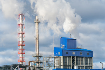 Factory with Smoking pipes on the background of gray-blue sky in Sunny weather. Concept of environmental pollution and ecology
