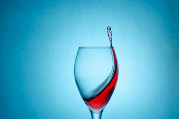Beautiful splashes, drops of red wine in a glass on a blue background close-up with a copy of the space. Freezing liquids in motion.