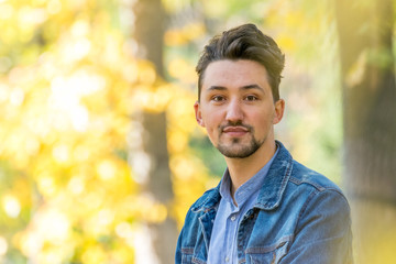 Handsome young man looking at the camera. Portrait of a confident and successful young man with a denim jacket and blue shirt outside. Happy guy smiling