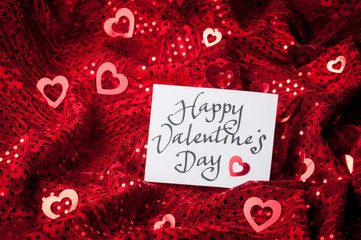 Handwritten Happy Valentine's Day message in informal calligraphic script on white card sitting on sparkly red heart background