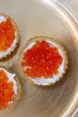 three tartlets with cream cheese and red caviar on a gold plate. the concept of a delicious Breakfast, buffet and snack. seafood dish. the view from the top. space for text.