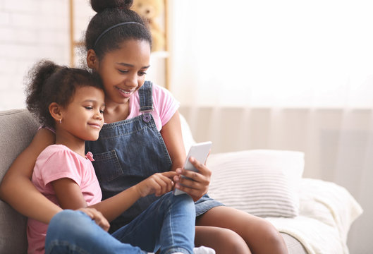 Little african american girl playing on her sister's cellphone