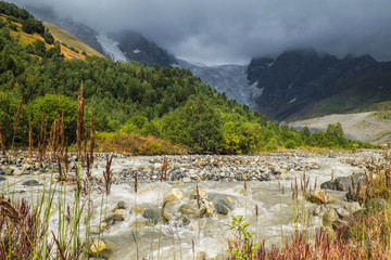 Strong mountain rocky river Adishchala and its source glacier Lardaad on a background in gloomy light