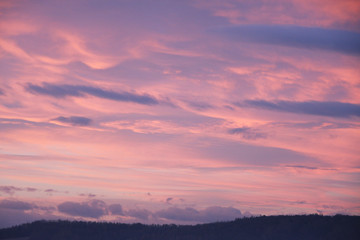 Fototapeta na wymiar Dreamy evening sky in pastel tones with fluffy pink clouds at sunset over silhouette of hill country