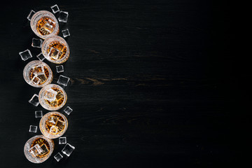 many glasses of whiskey with ice on a black table