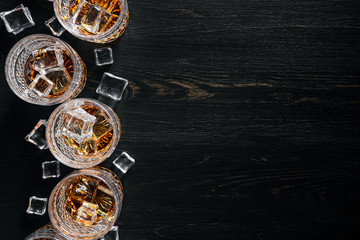 many glasses of whiskey with ice on a black table