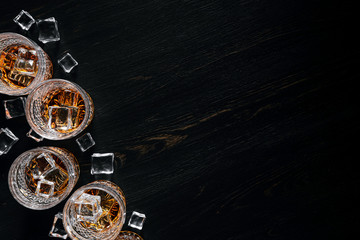 many glasses of whiskey with ice on a black table