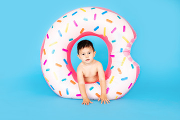 Happy baby boy in swimsuit with swimming ring donut on a colored blue background