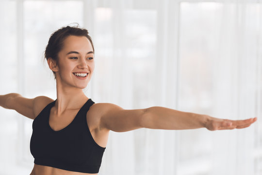 Woman Exercising Yoga In Warrior Pose In Modern Studio