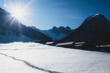 Sunflare over snow covered mountain slope and chalets.