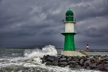 Obraz premium Lighthouse on the pier in Warnemuende during storm the waves break on the pier - Baltic Sea in Germany