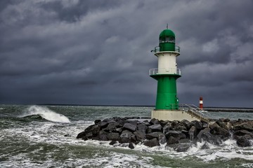 Fototapeta na wymiar Lighthouse on the pier in Warnemuende during storm the waves break on the pier - Baltic Sea in Germany