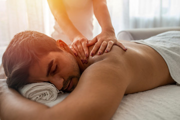 Young man is enjoying massage on spa treatment. Man relaxing in a wellness center. Young man receiving massage at spa salon. Hands of a masseuse working. Handsome man at the spa