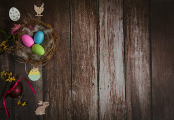 Easter composition. Nest with colored eggs, wooden decorative Easter figurines and forsythia branches on a wooden background. Free space.