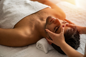 Relaxed man receiving an anti-stress temple massage. Close-up of a man receiving facial massage at the spa. Close-up of a man relaxing with eyes closed during head massage at the spa.