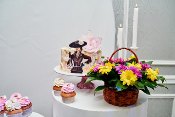 Candy bar served with cake, pink cupcakes, bouquet of flowers in basket and candles on round table, copy space. Dessert table for party. Holiday or birthday concept