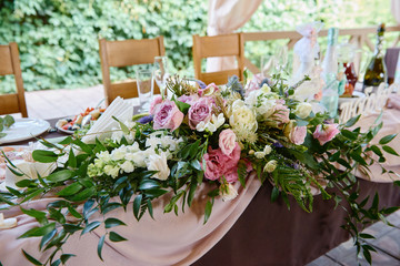 Lush floral arrangement on wedding table outdoors. Wedding presidium in restaurant, copy space. Banquet table for newlyweds with pink and purple rose flowers. Luxury wedding decorations